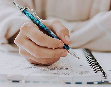 Vertical selective closeup of a female writing in a notebook with a blue pen